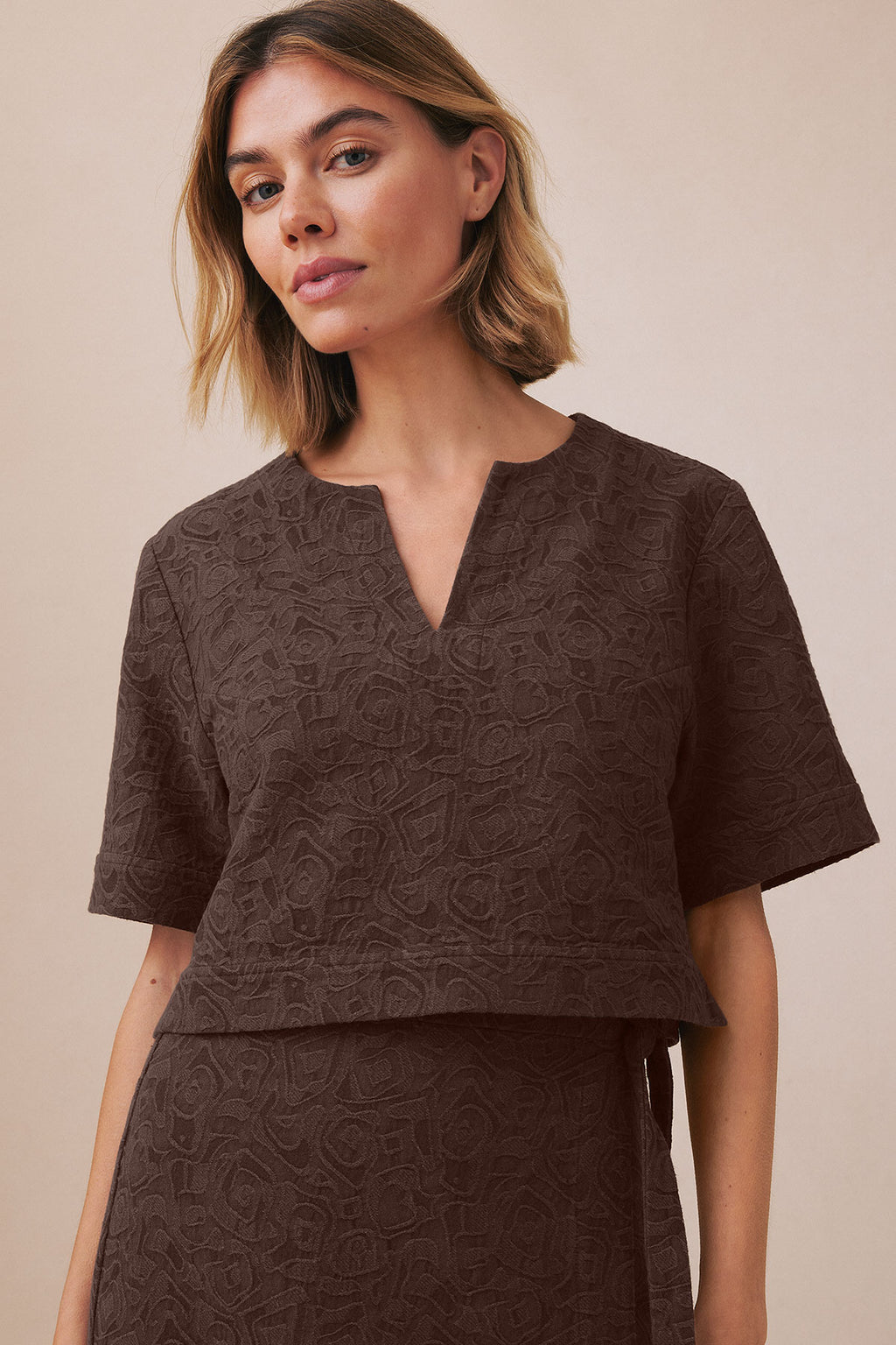 Woman wearing cocoa brown jacquard popover top with matching skirt, V-neckline and short sleeves.
