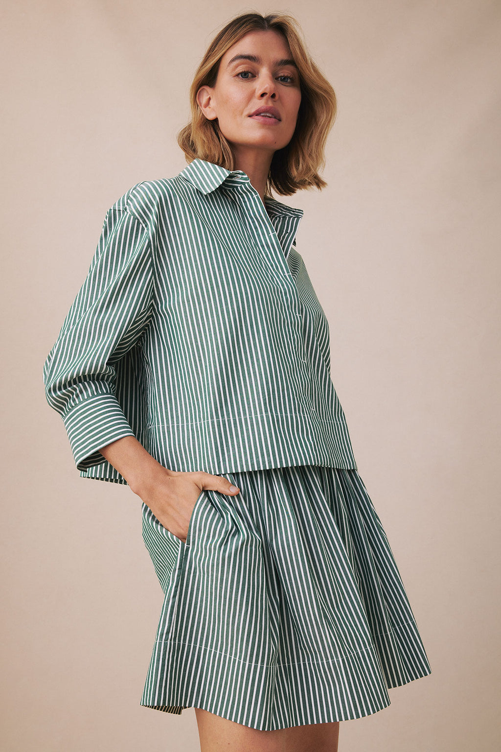 Woman wearing hunter green and white vertical striped button-up shirt and matching pleated skirt with pockets.