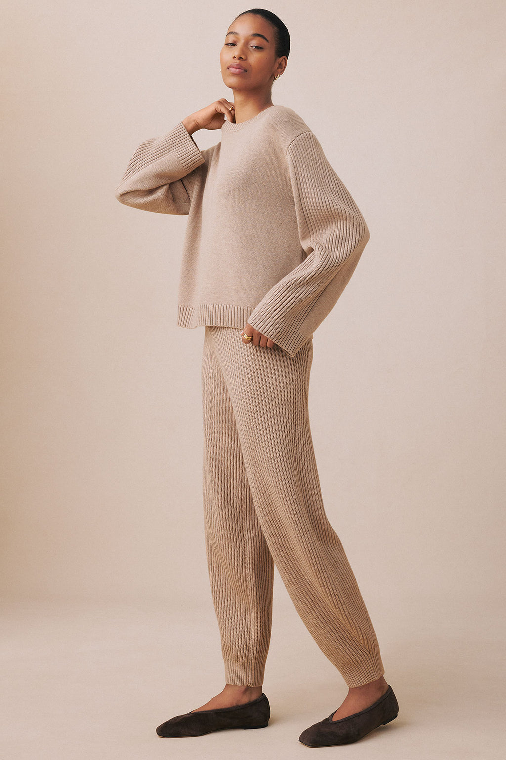 Person wearing fawn heather ribbed knit sweater with matching ribbed jogger pants and black slippers.