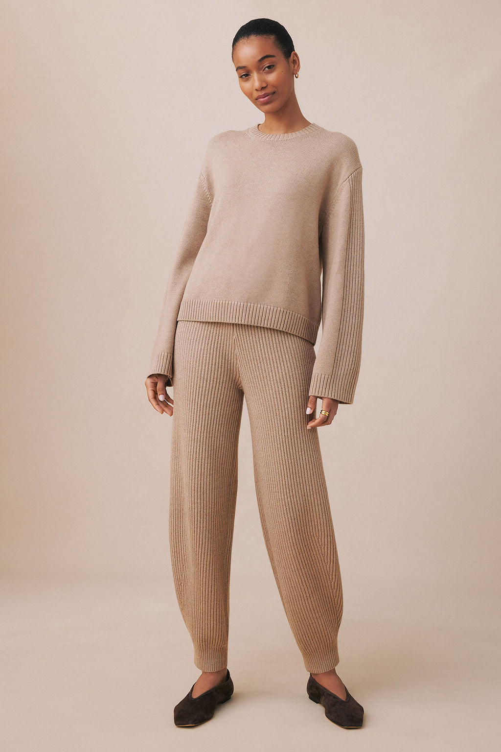 Woman wearing fawn heather ribbed knit sweater and matching ribbed jogger pants with black slip-on shoes.