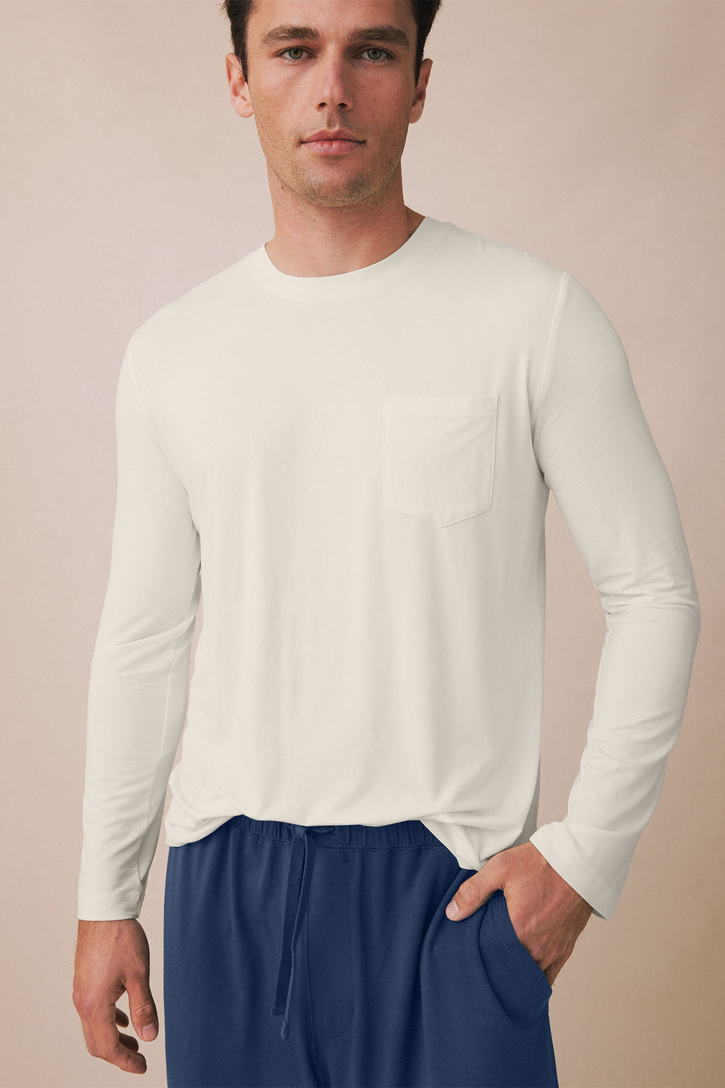 Man wearing cream long-sleeve shirt with chest pocket and navy drawstring pants.
