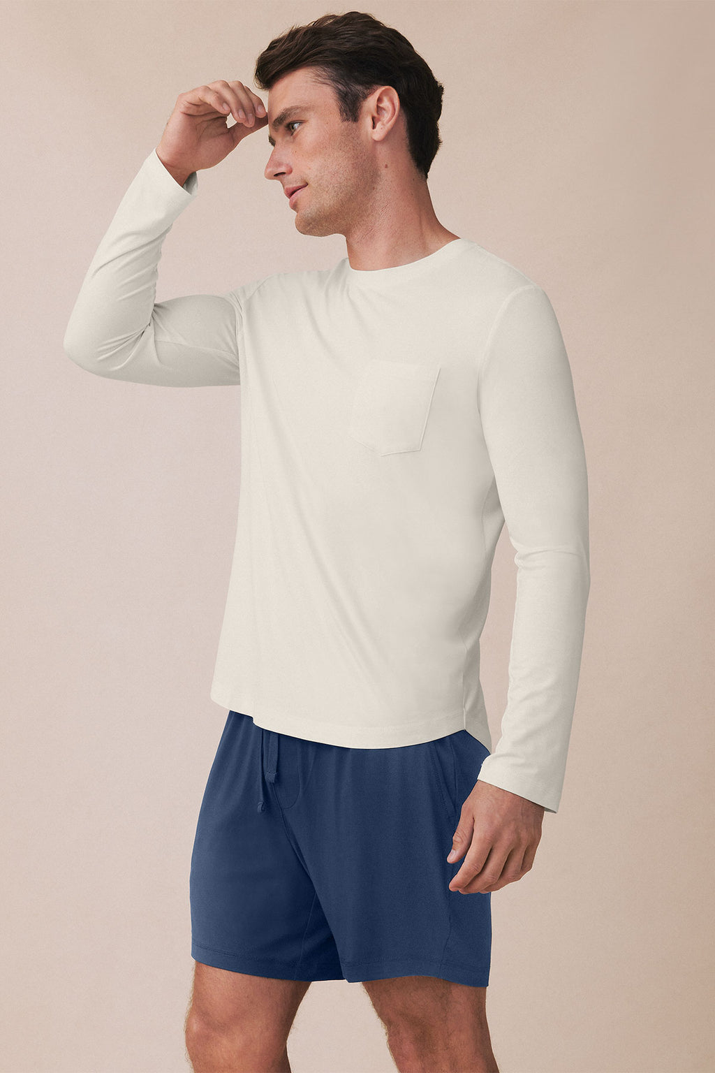 Man wearing cream long-sleeve shirt with chest pocket and navy shorts.