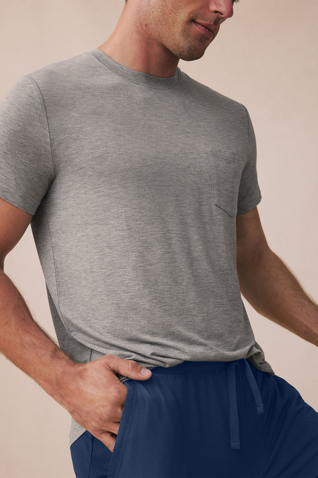 Man wearing gray short-sleeve t-shirt and navy drawstring pants against beige background.