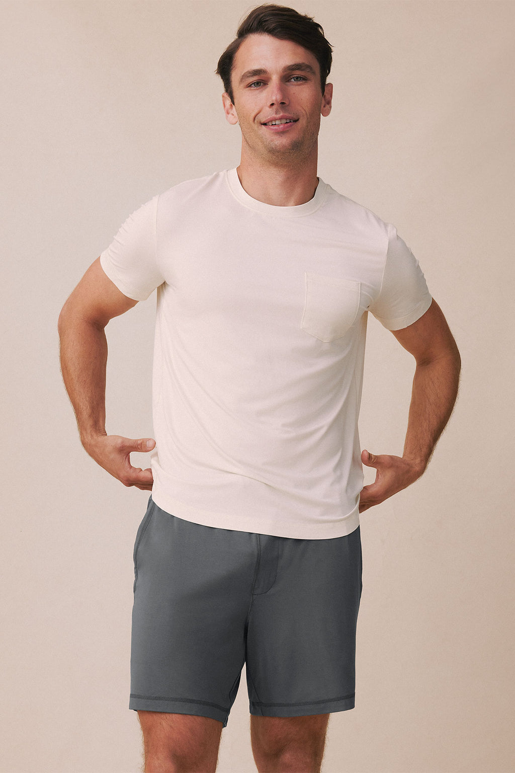 Man wearing cream short-sleeve t-shirt with chest pocket and gray shorts.