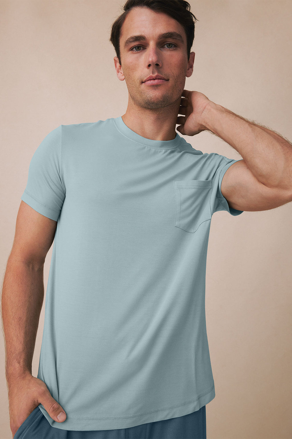 Man wearing light blue short-sleeve t-shirt with chest pocket and blue shorts against neutral background.