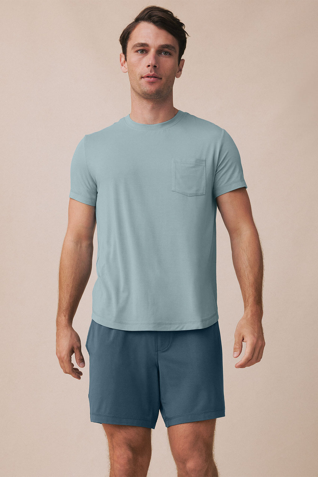 Man wearing light blue-gray t-shirt with chest pocket and dark teal shorts.