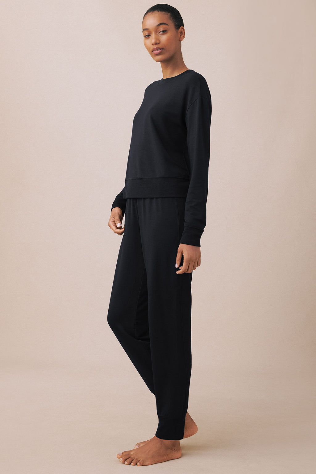 Woman wearing black long-sleeve crewneck sweatshirt and matching black jogger pants with elastic cuffs.