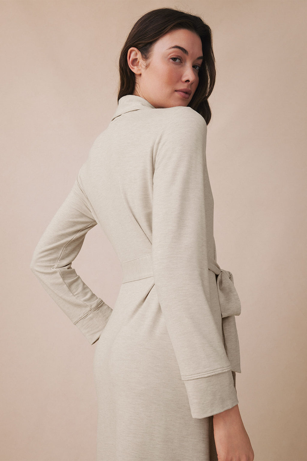 Woman wearing a light beige robe with a collar, long sleeves, and tie waist, shown from the back.