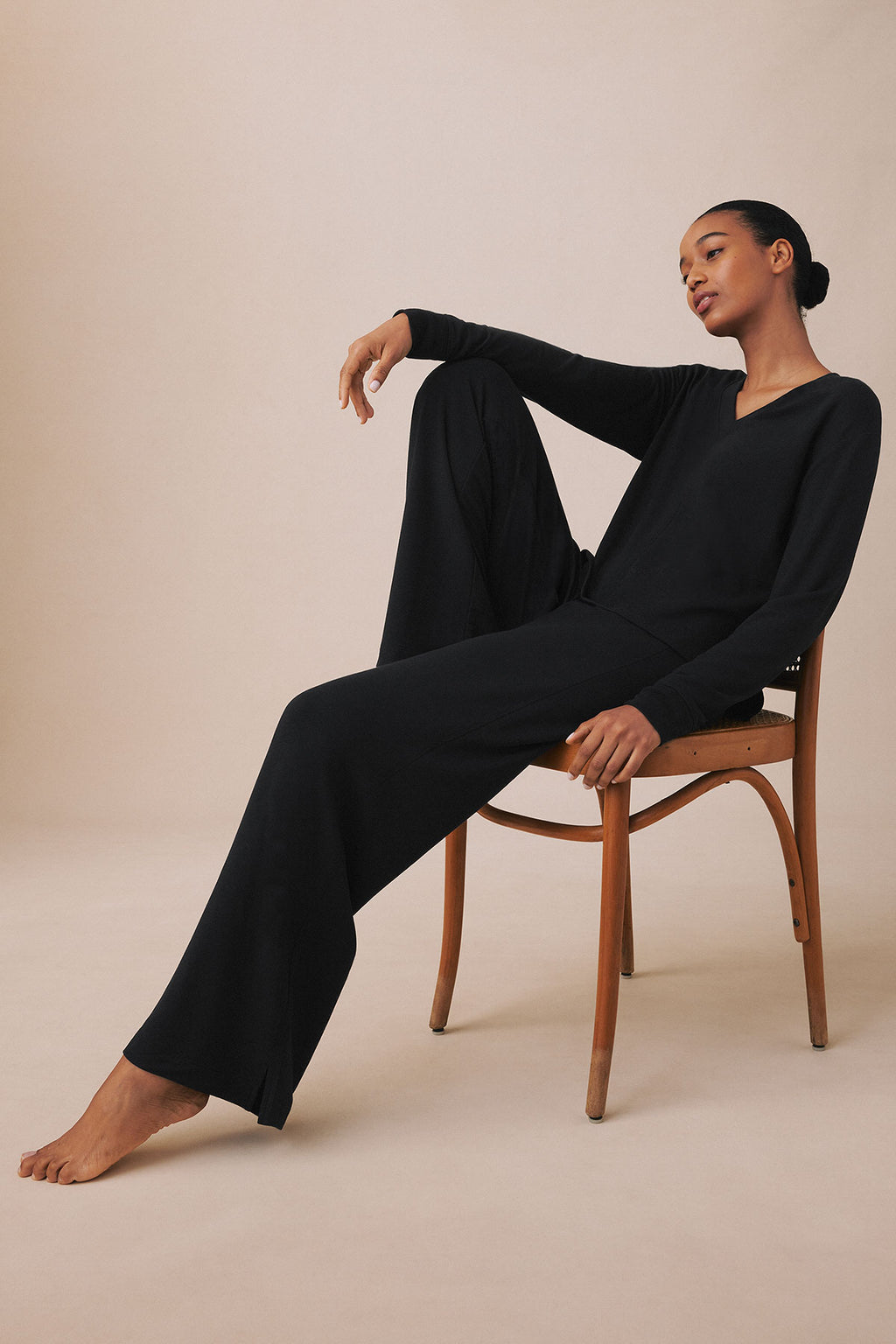 Black long-sleeve V-neck top and matching wide-leg pants worn by model seated on wooden chair.