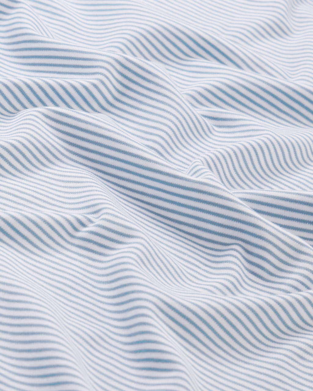 Close-up of soft white Pima cotton with thin, light blue stripes and gentle folds—featured in our Mens Pima Sleep Shorts in Anchor Blue Bar Stripe.