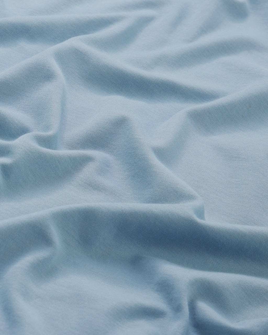 Light blue fabric with soft folds creates a textured, smooth surface that appears slightly stretchy—similar to the Peruvian cotton used in the Mens Pima Crewneck Tee in Anchor Blue.