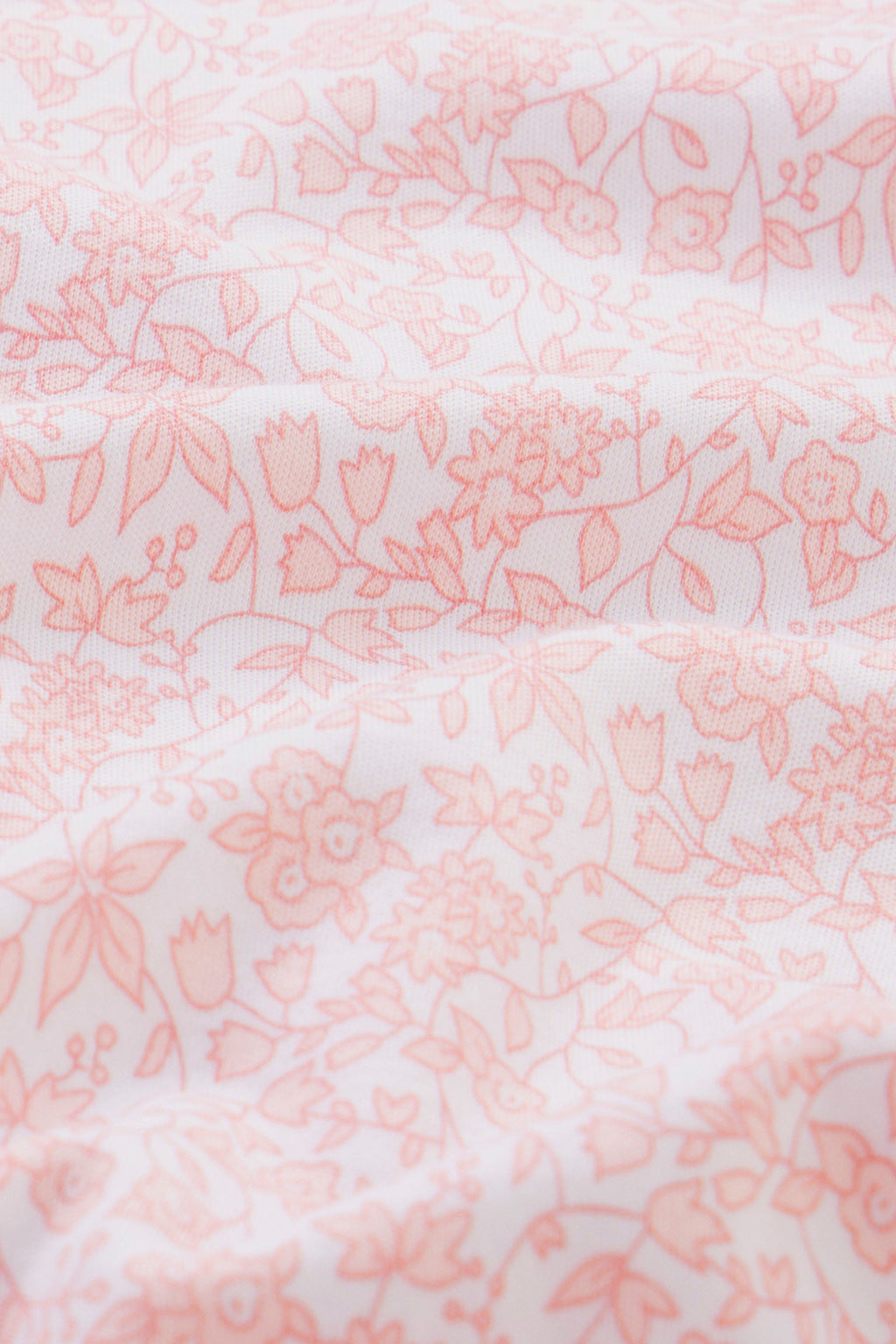 Close-up of the Reversible Baby Blanket in English Rose Multi, featuring a delicate, light pink floral pattern on white. Soft folds and texture highlight its gentle charm.