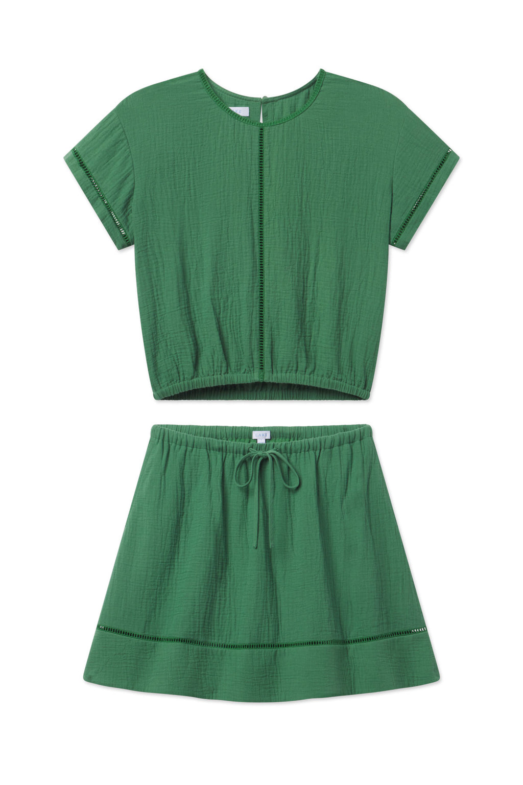 The Cabana Skirt Set in Palm features a two-piece design with a short-sleeve cropped top and high-waisted skirt, both in emerald green textured fabric with subtle cut-outs and a drawstring waist for comfort.