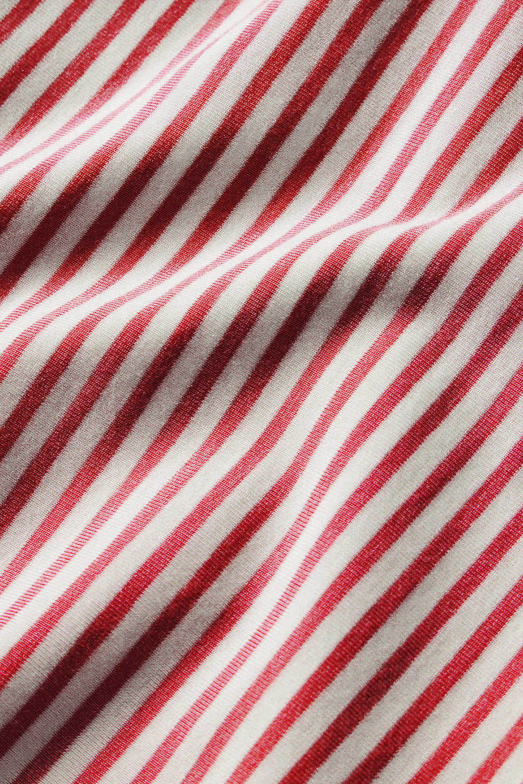 Red and white diagonal striped fabric with varying shades of red stripes and cream-colored background.