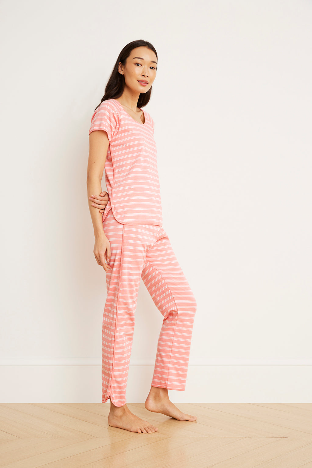 Woman wearing coral and white striped short-sleeve top and matching full-length pajama pants.