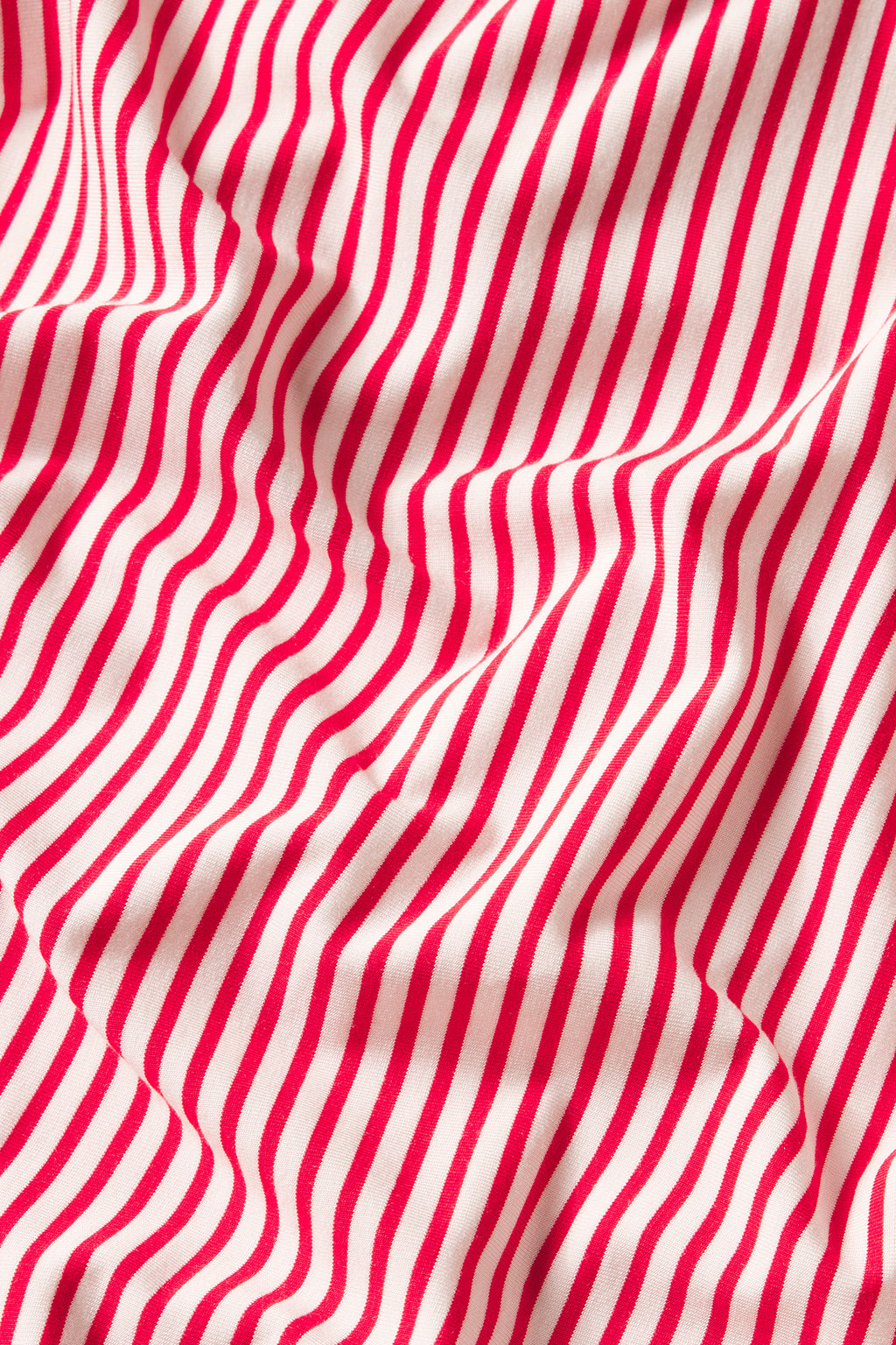 Close-up of fabric with red and white diagonal stripes, featuring soft folds. The dynamic drape mimics the design style of the DreamModal Kimono Pants Bundle in Ski Patrol Pencil Stripe.