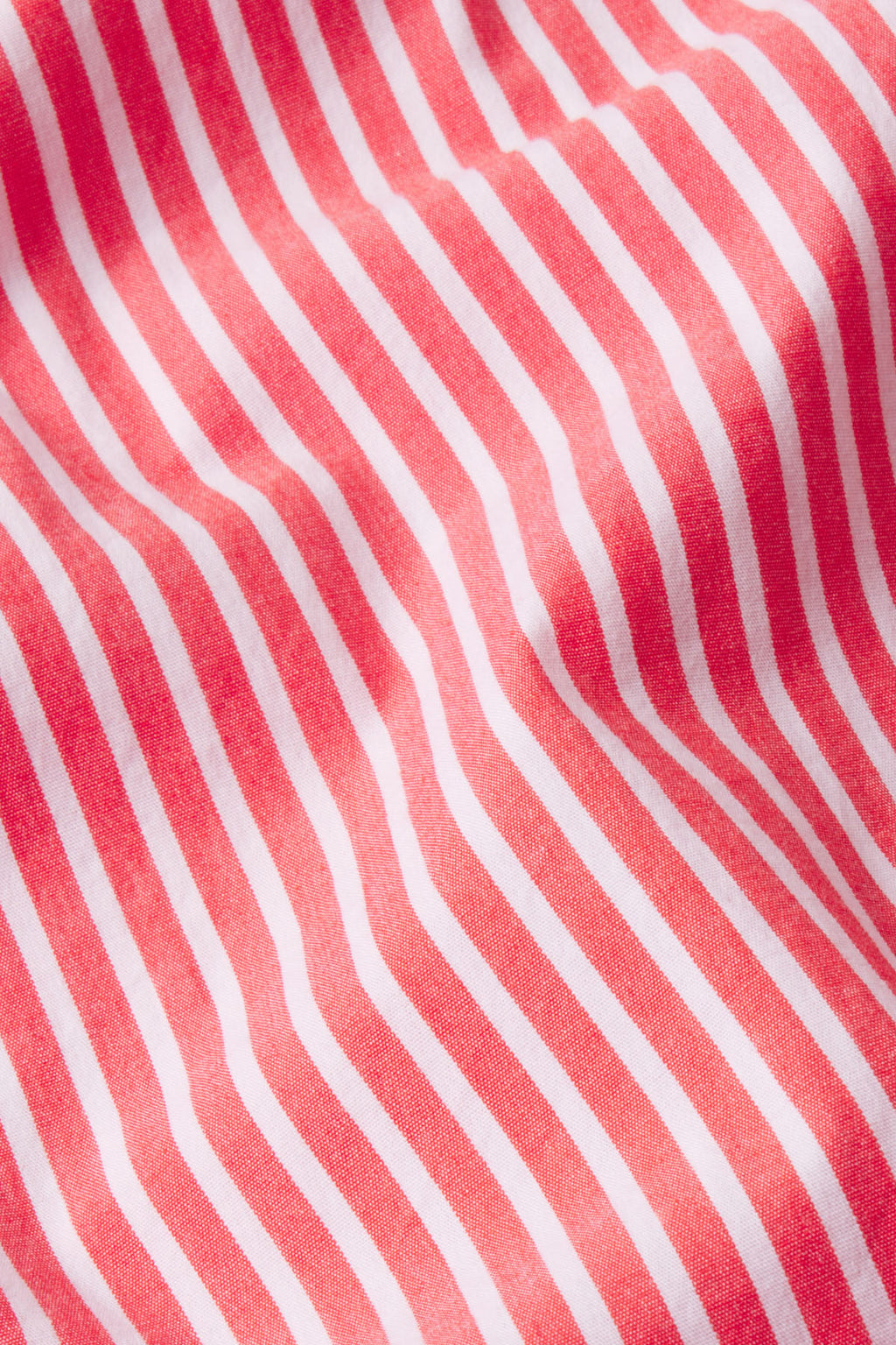 Close-up of the Sunday Dress in Tart Bengal Stripe, featuring red and white diagonal stripes on cotton poplin with soft folds and gentle shadows for a textured look.