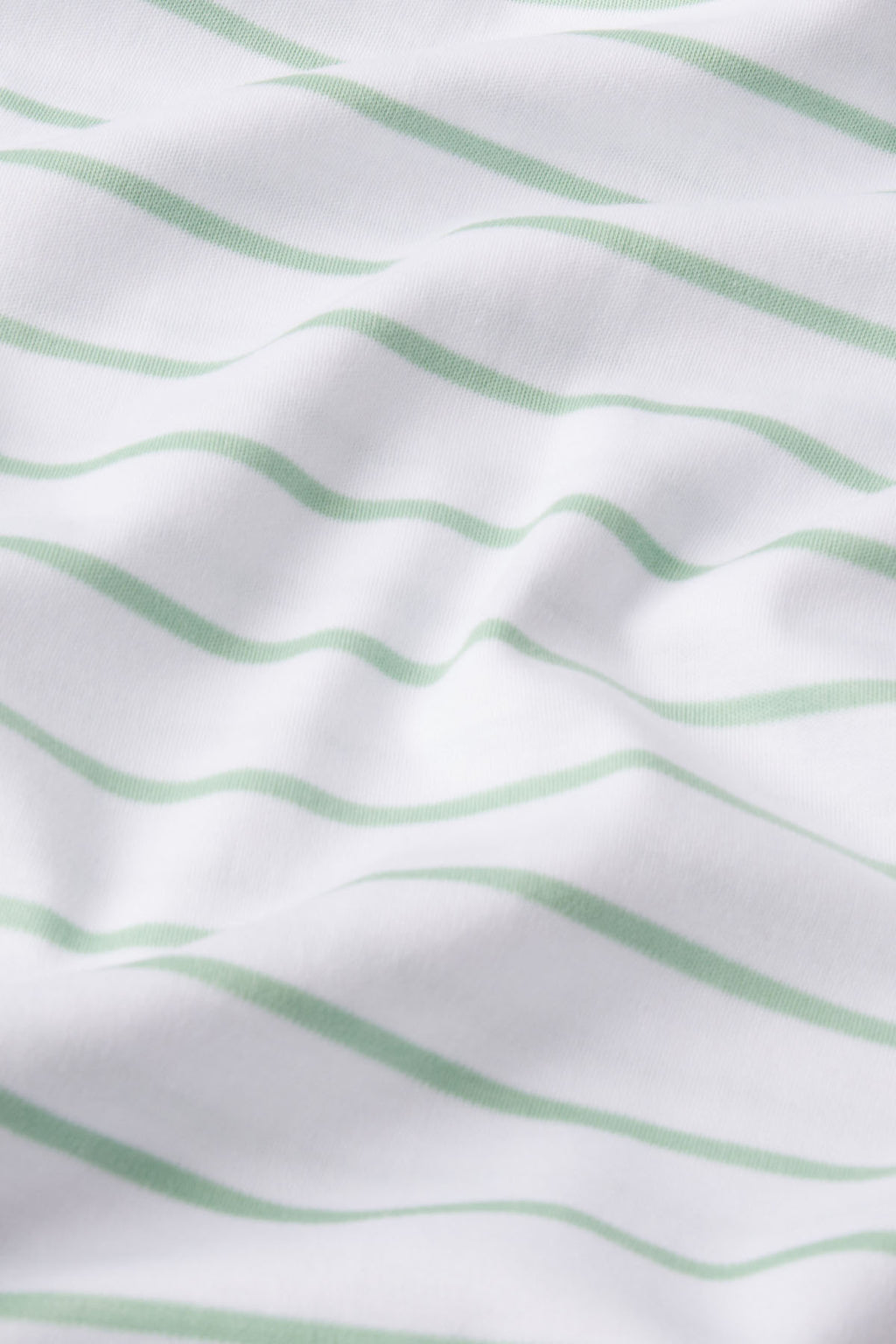 White fabric with soft, light green horizontal stripes and gentle wrinkles creates a textured look, making the Pima Shorts Set in Parisian Green Club Stripe perfect for breathable, cozy sleepwear.