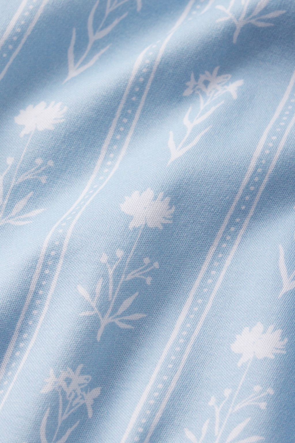The Pima Short Robe in French Blue Watercolor Stems features light blue 100% Pima cotton with a white floral pattern and vertical dotted lines. Delicate flowers and a slight texture give it a soft, airy appearance.