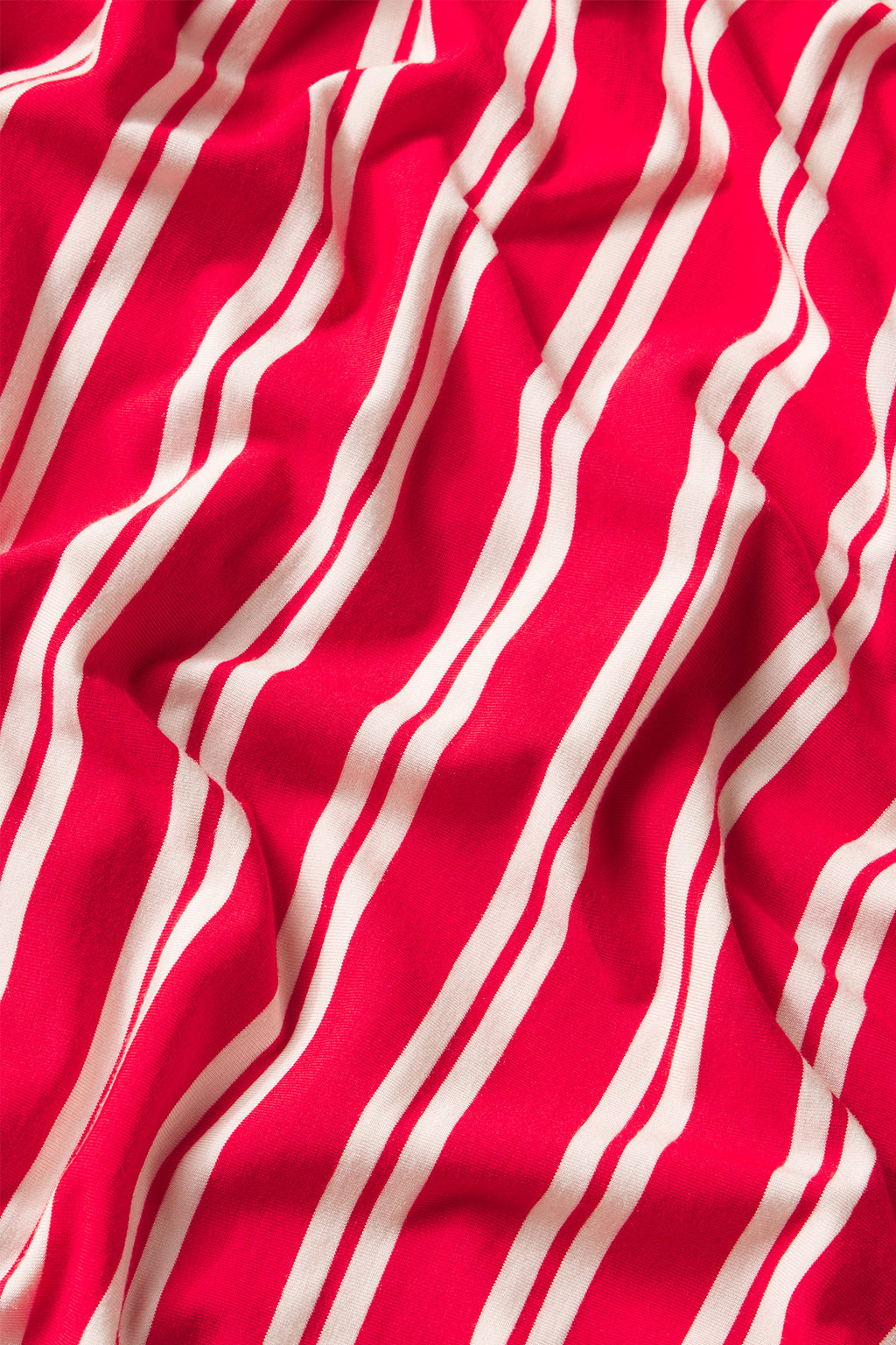 Crumpled fabric with a bold red background and white Ski Patrol Stripe running diagonally, inspired by the DreamModal Daydream Pants Set in Ski Patrol Stripe.