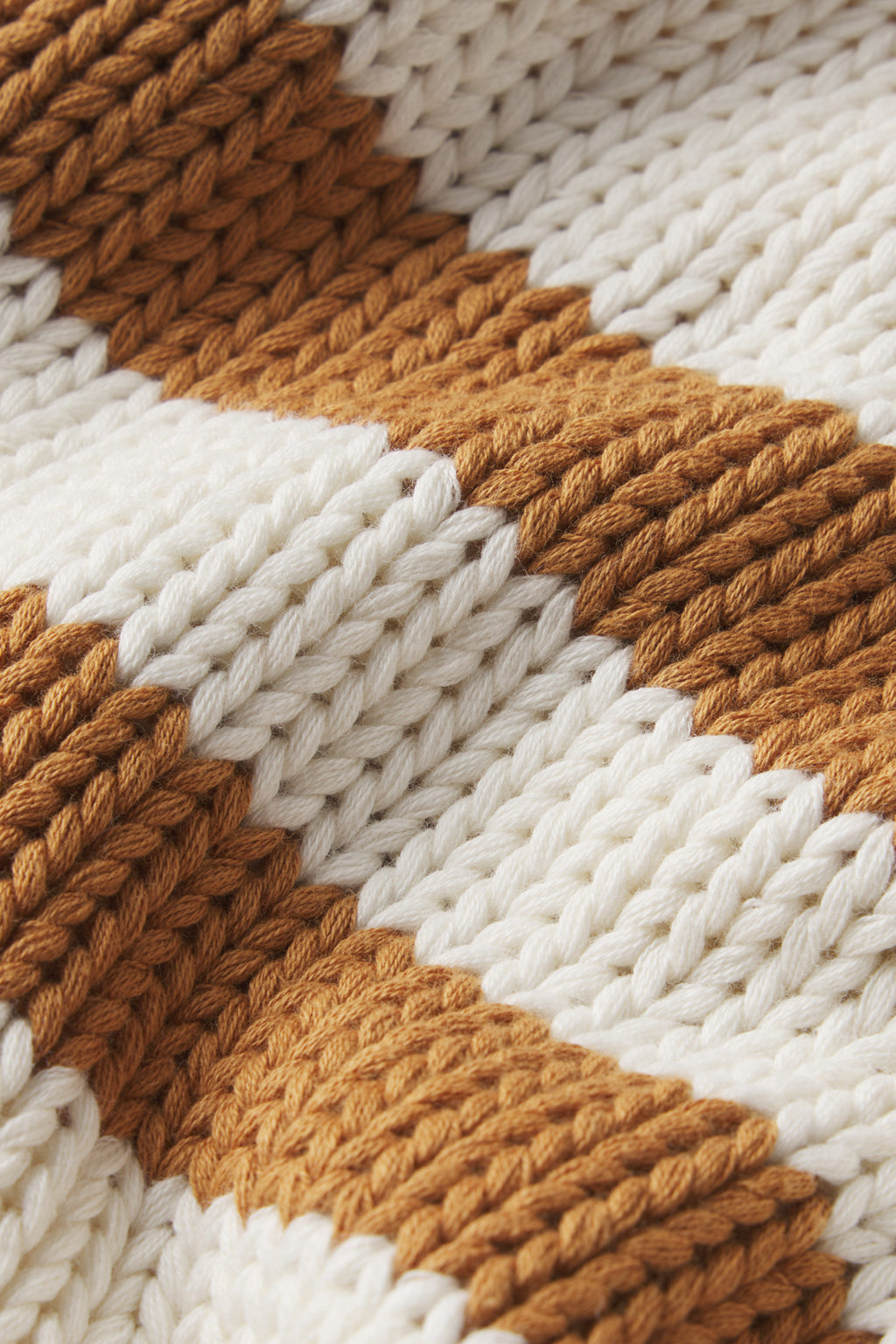 A close-up of the Jane Cotton Sweater in Cognac Double Stripe shows chunky cotton knit with alternating thick white and cognac stripes, highlighting its detailed texture and stitch pattern.