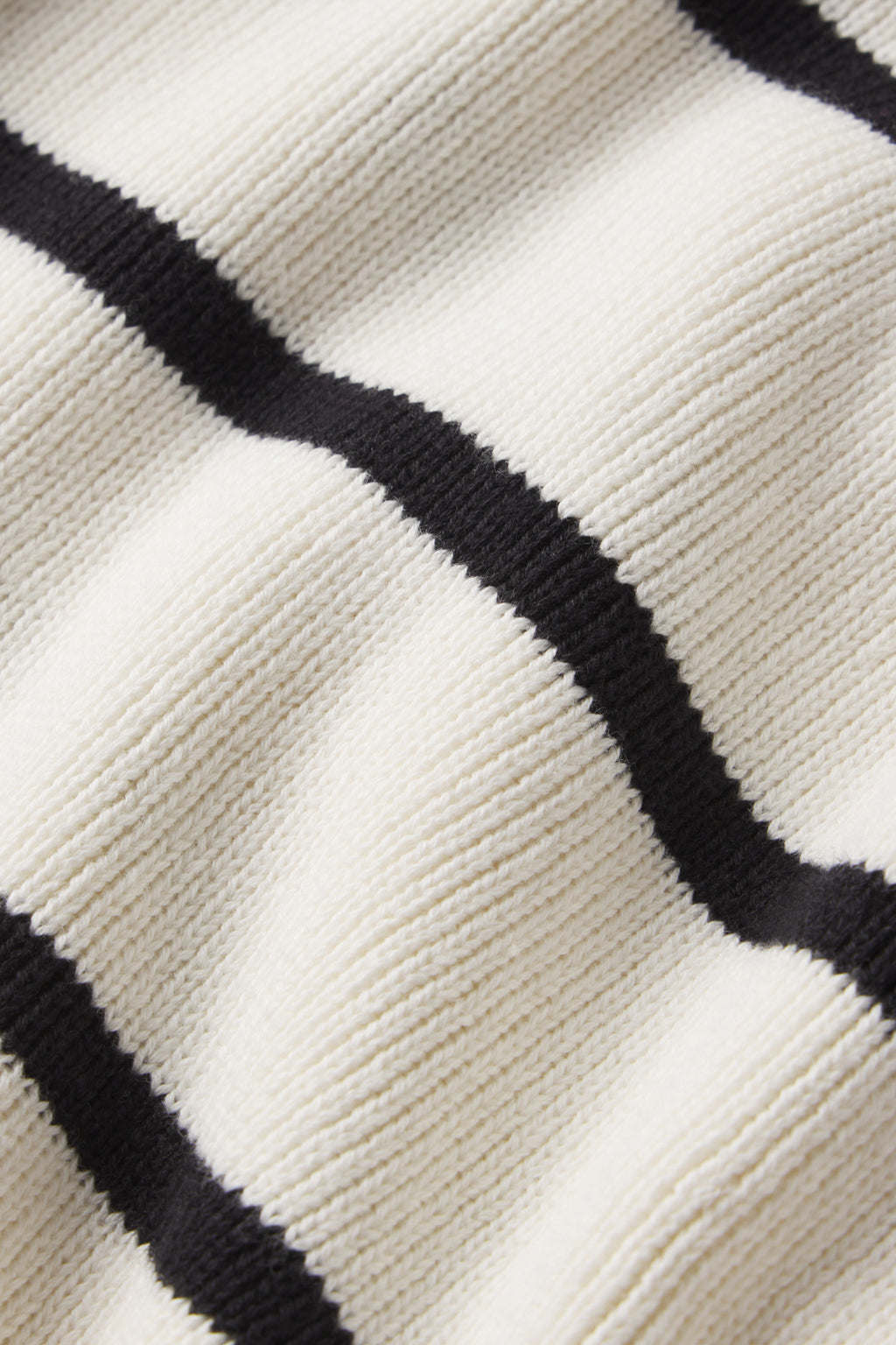 Close-up of the Madeline Sweater in Ivory Black Stripe, made from 100% cotton knitted fabric with wide horizontal stripes on a textured off-white background.
