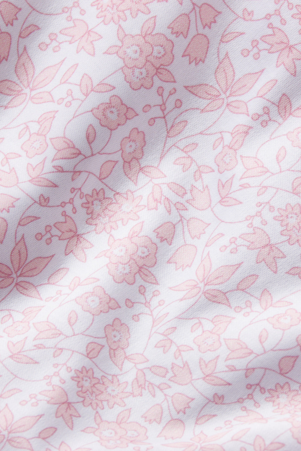 Close-up of the Baby Sleeper in English Rose Garden Floral, crafted from 100% Pima cotton and adorned with delicate pink flowers, leaves, and stems. Gentle shadows highlight its soft texture—perfect for your little one.