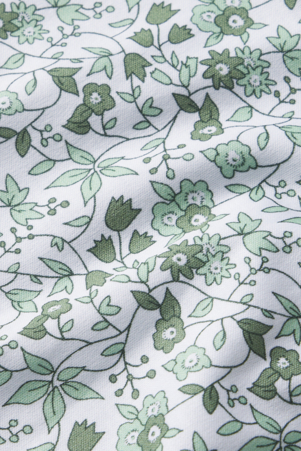 Close-up of Pima cotton fabric in Topiary Garden Floral, shown with soft folds and textured shadows. The repeating green botanical design matches the style of our Pima Crew Short-Long Set in Topiary Garden Floral.