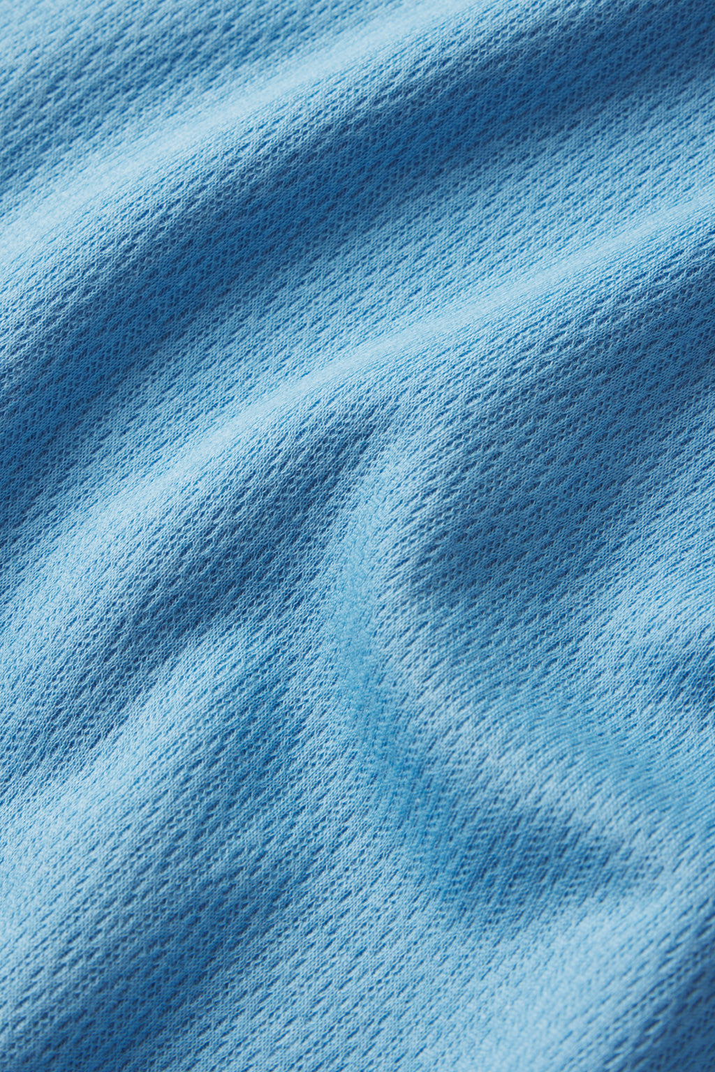 Close-up of light blue textured fabric from the Pointelle Maternity Wide Leg Tank Set in Serene Blue, showing the pointelle weave and gentle folds that create soft shadows and highlights on the surface.