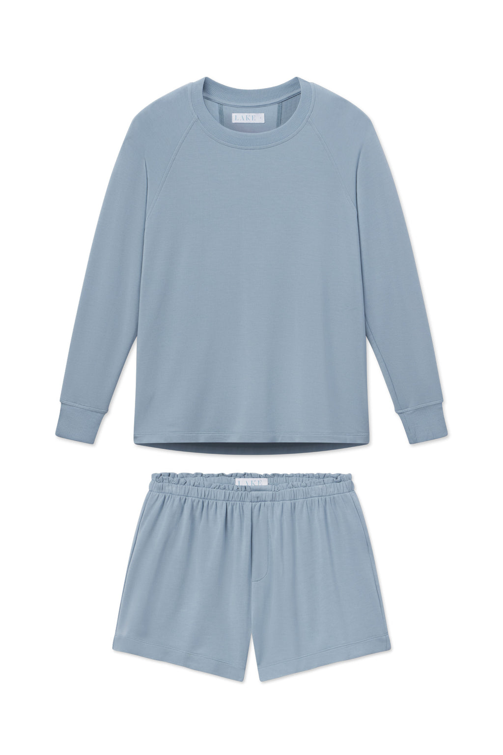 Relax Shorts Set in Dusty Blue includes a light blue long-sleeve pajama top and matching elastic-waist shorts, made from soft fabric. Cozy and comfortable, this set is perfect for lounging. Shown laid flat on a white background.