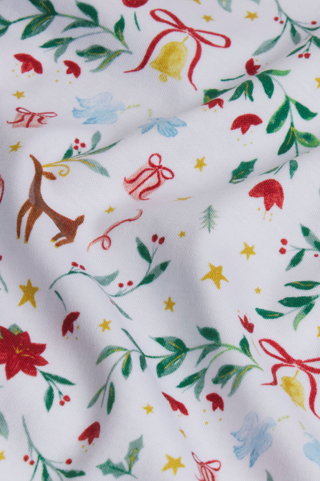 White Pima cotton fabric with holiday print including reindeer, bells, bows, stars, holly leaves, and poinsettias in red, gre