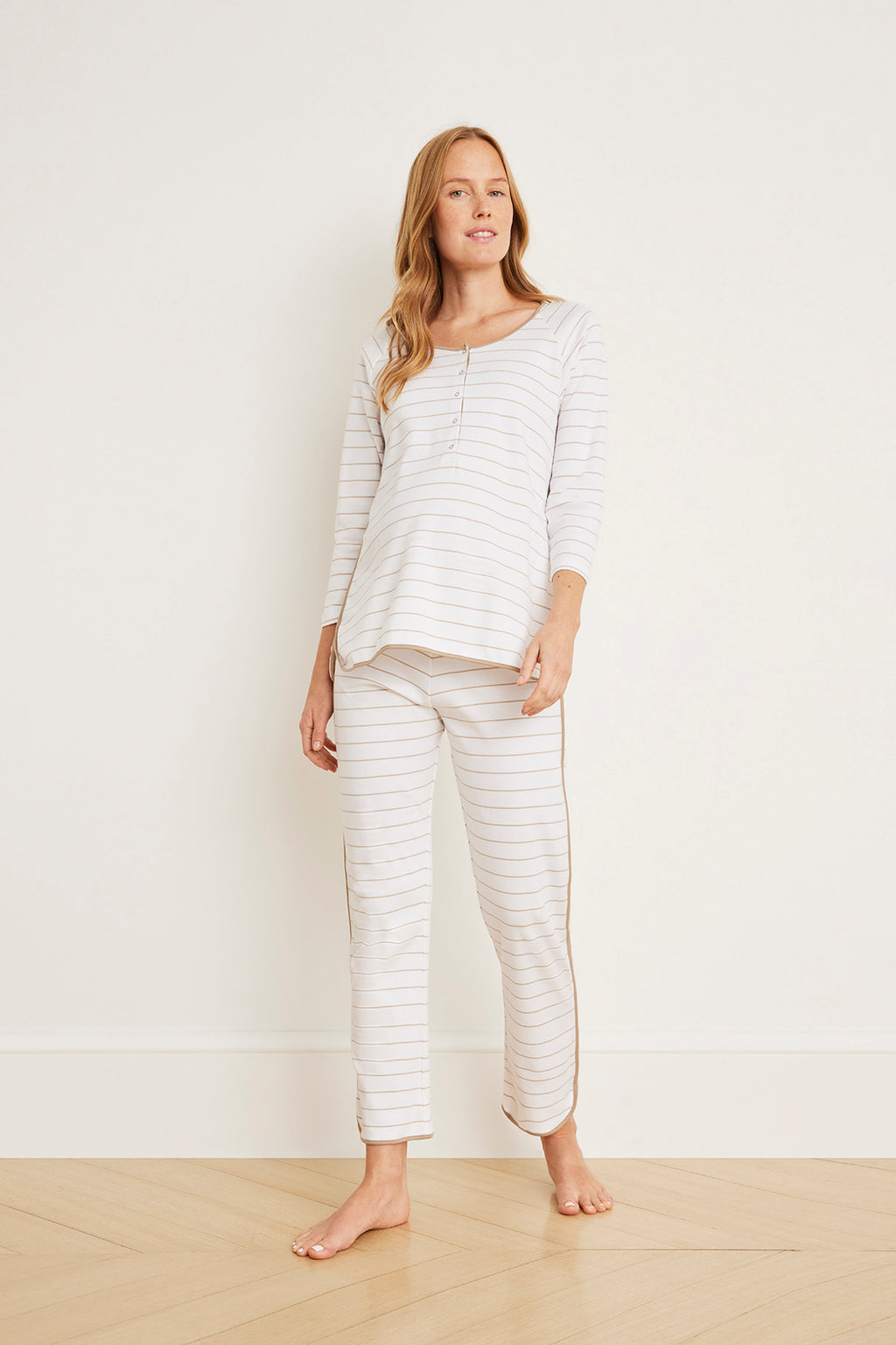 Woman wearing a cream and tan striped long-sleeve maternity top with matching striped pants, standing barefoot.