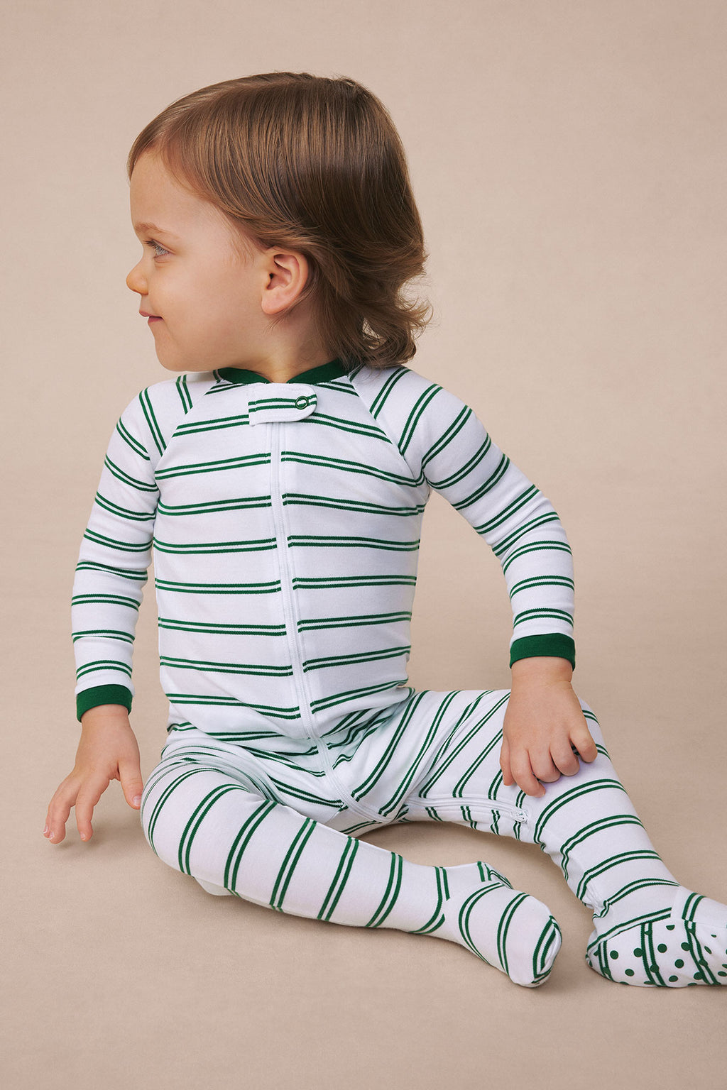 Toddler wearing white sleeper with green horizontal stripes and matching striped socks, shown from back view.