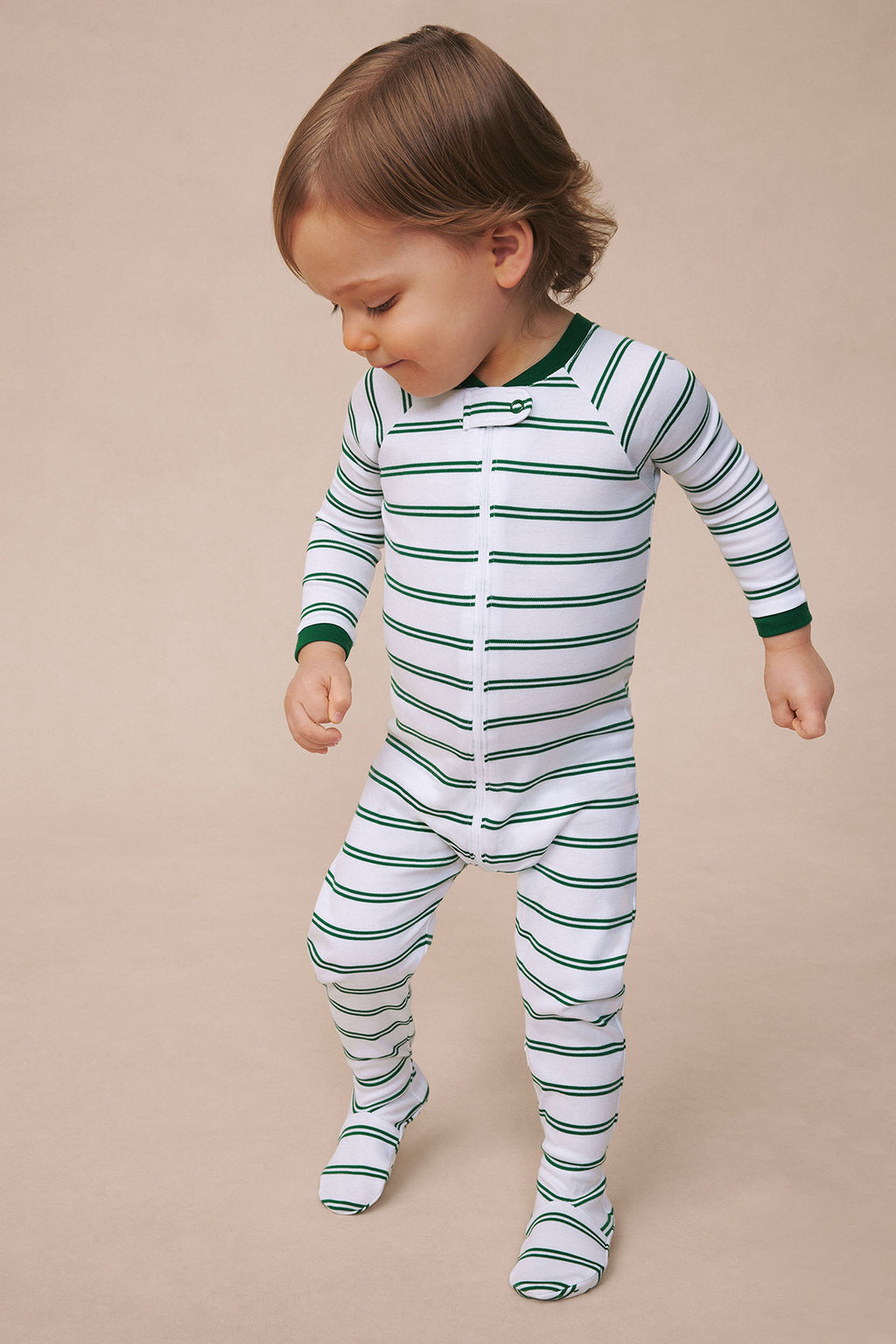 Toddler wearing white sleeper with green and navy horizontal stripes and front button closure.