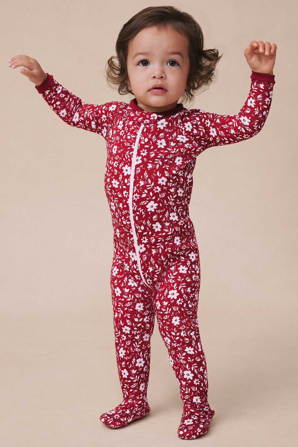 Toddler wearing garnet red long-sleeved sleeper with white floral and leaf pattern, front zip closure.