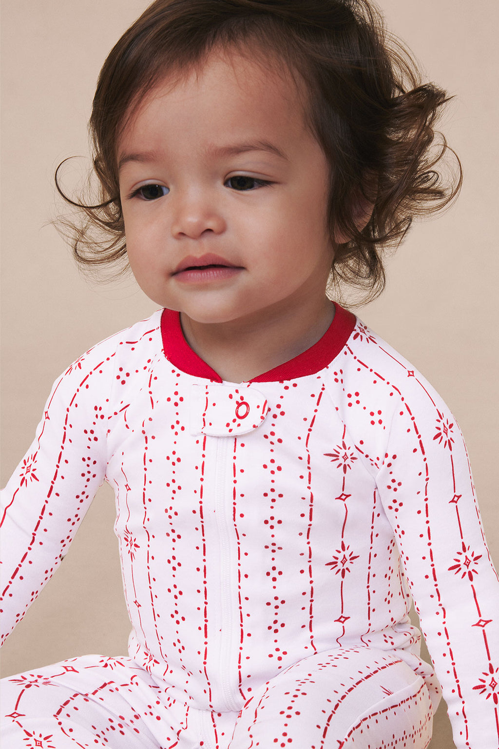 Toddler wearing long-sleeve sleeper with red and white striped pattern and geometric designs, red ribbed neckline.