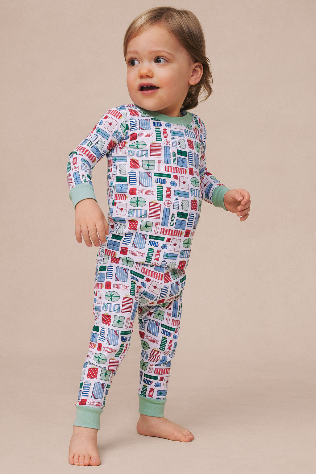 Toddler wearing long-sleeve pajama set with colorful geometric print and sage green cuffs and waistband.