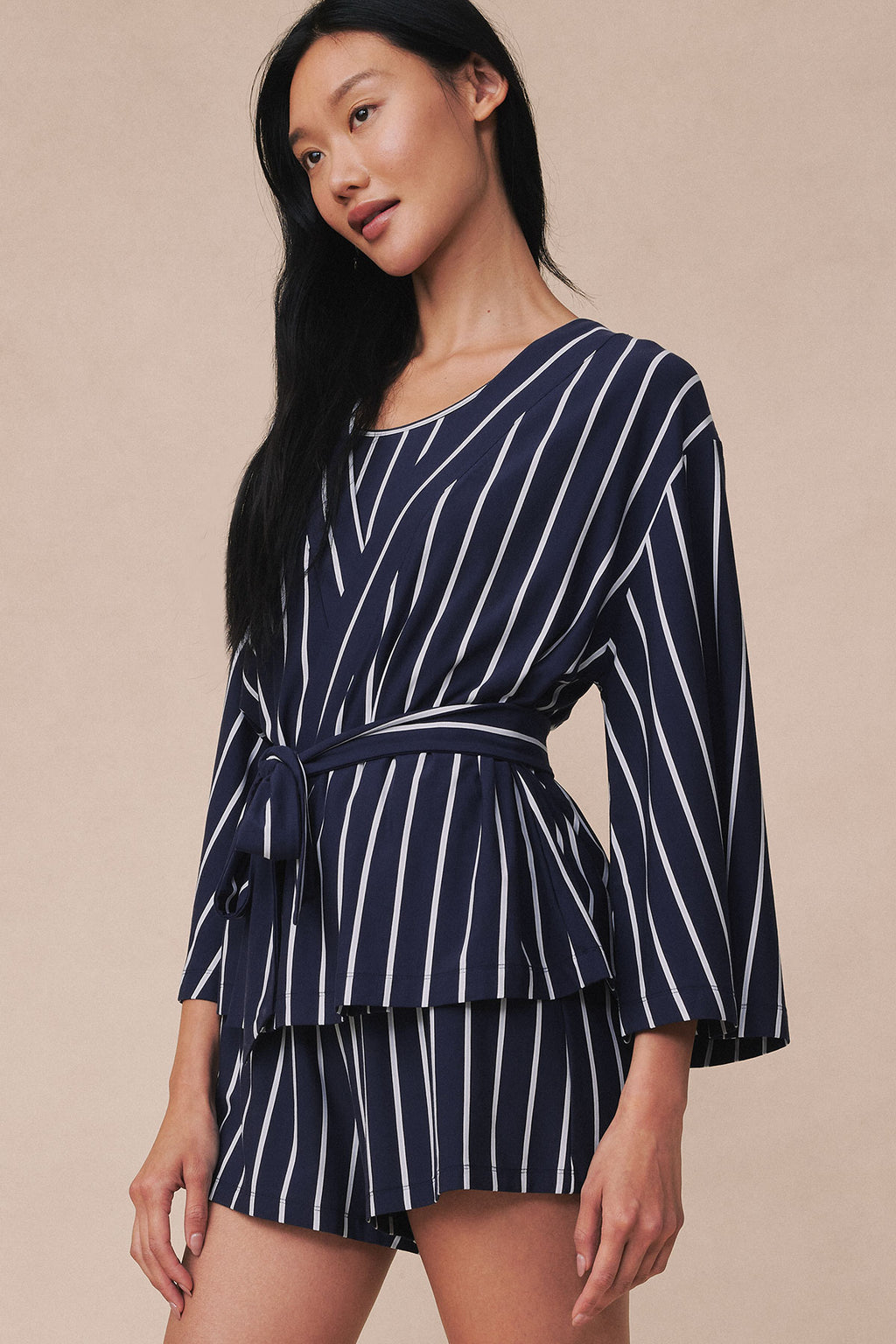 Woman wearing navy kimono with white vertical stripes and tie waist, paired with striped shorts.