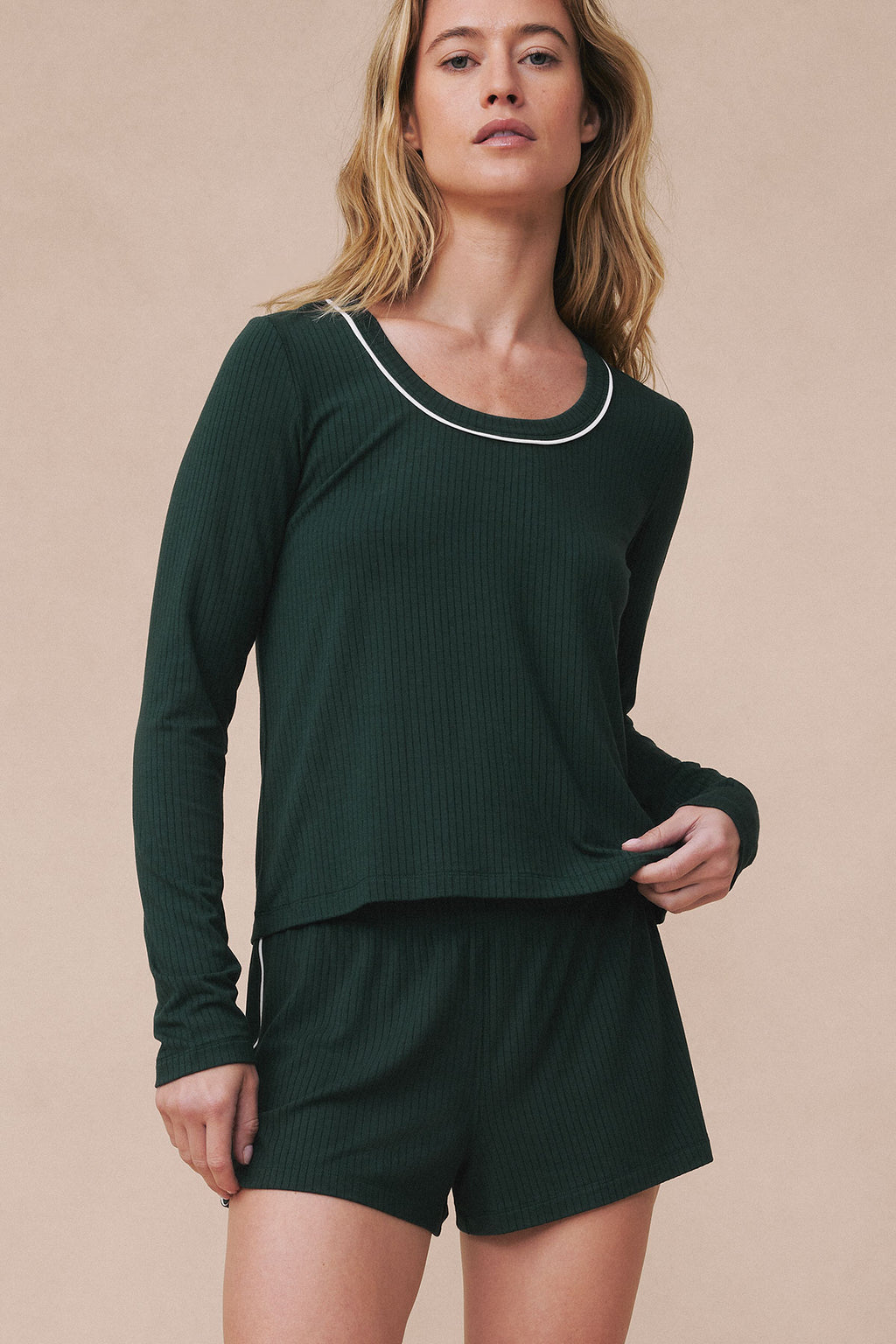 Woman wearing conifer green ribbed long-sleeve top with white neck trim and matching shorts.