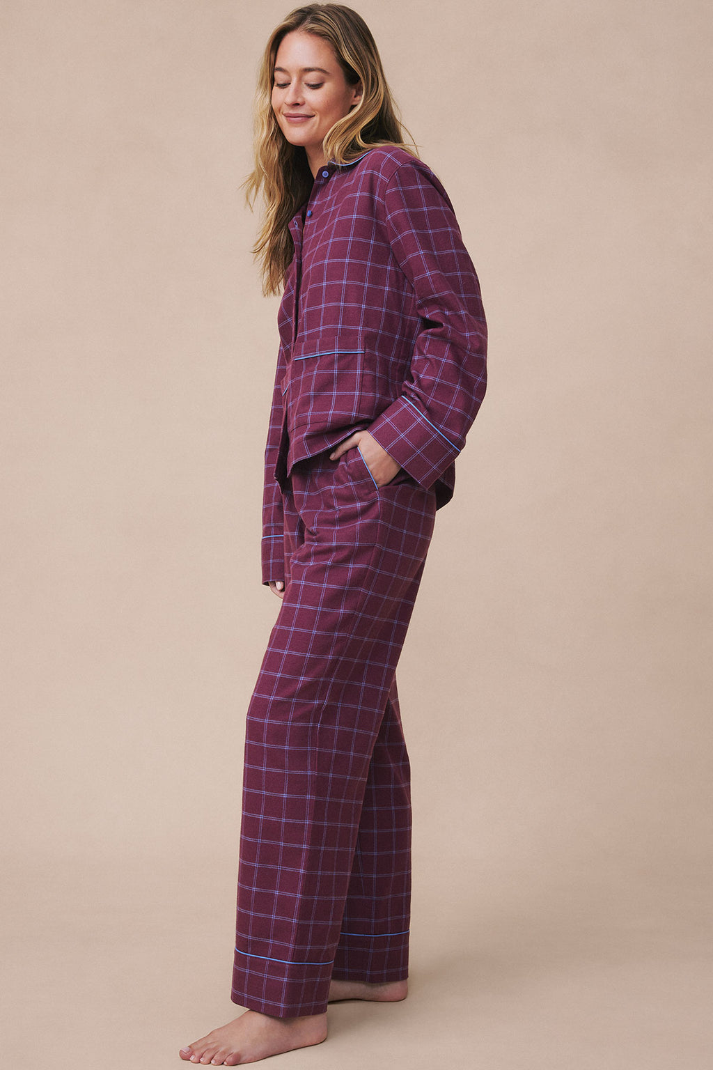Woman wearing burgundy windowpane flannel pajama set with button-up shirt and matching pants.