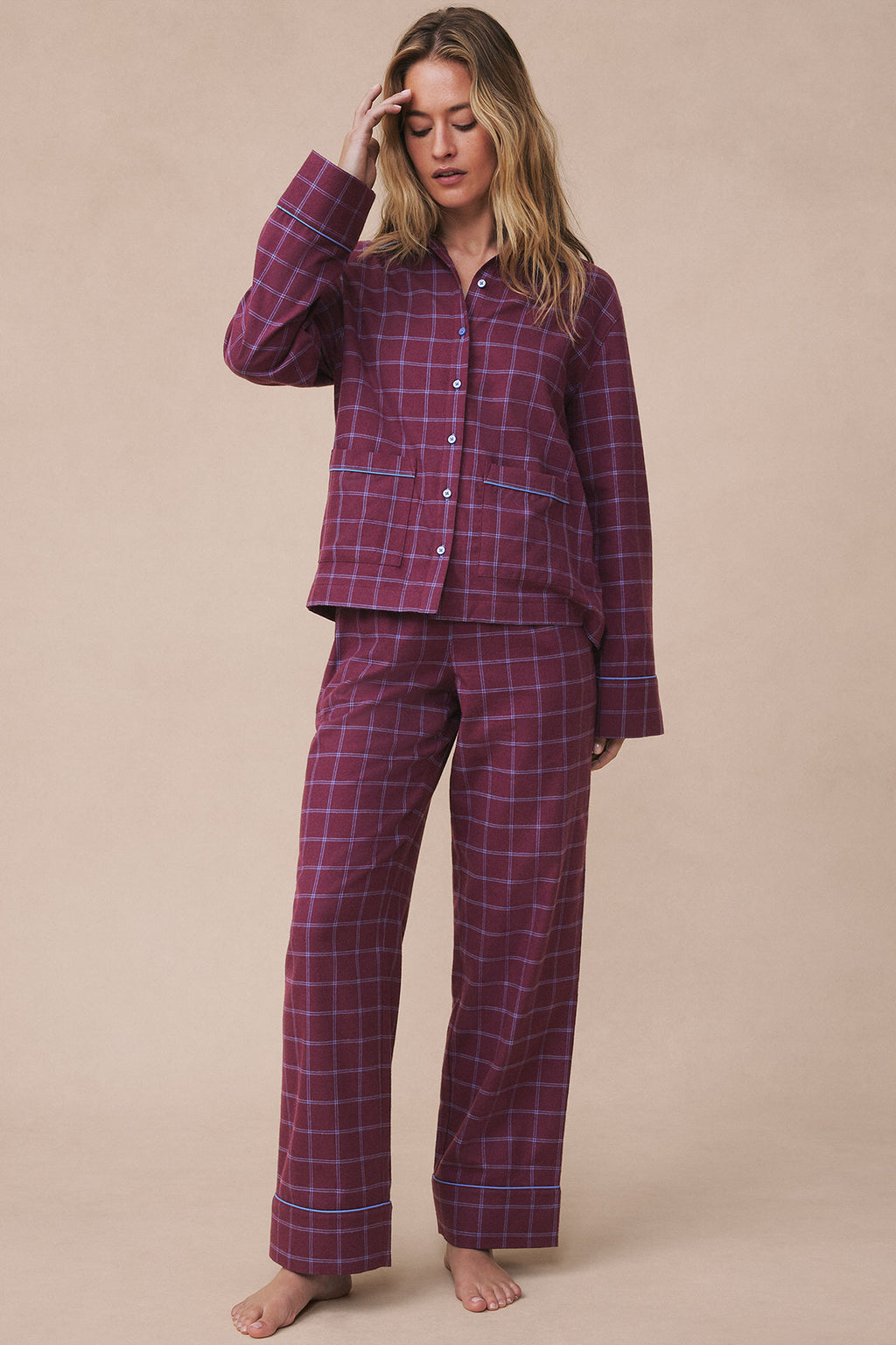 Woman wearing burgundy windowpane flannel pajama set with button-up shirt and matching pants.
