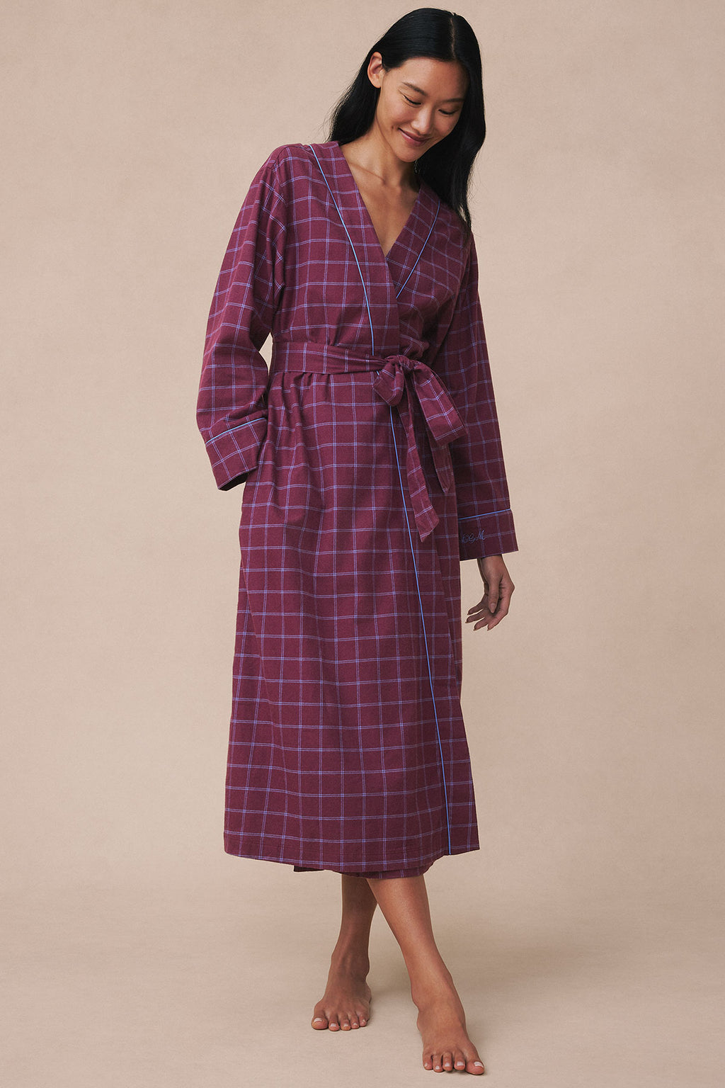 Woman wearing a burgundy windowpane plaid flannel robe with long sleeves and tie waist.