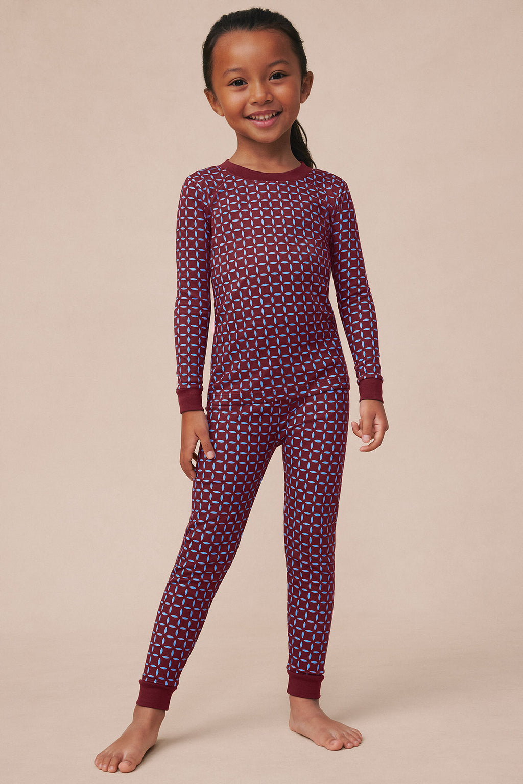 Child wearing burgundy long-sleeve pajama set with blue starburst pattern and ribbed cuffs.