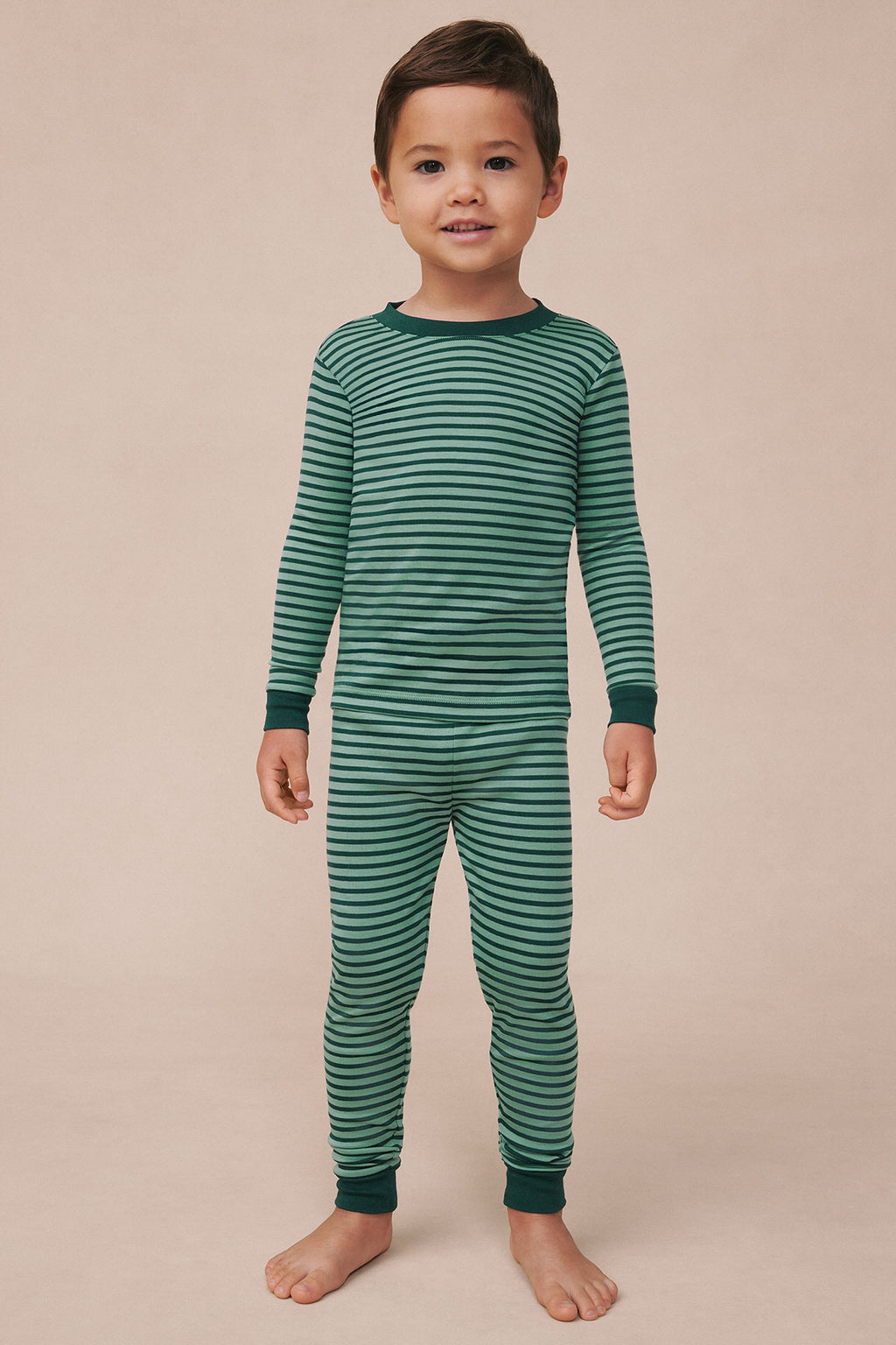 Child wearing long-sleeve striped pajama set in dark green and light green horizontal stripes with ribbed cuffs.