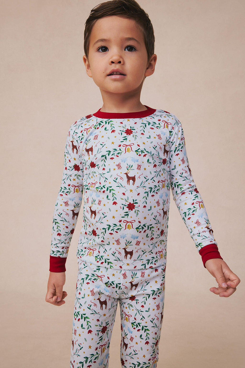 Child wearing light blue long-sleeve pajama set with red trim, featuring holiday-themed pattern with reindeer, presents, and 
