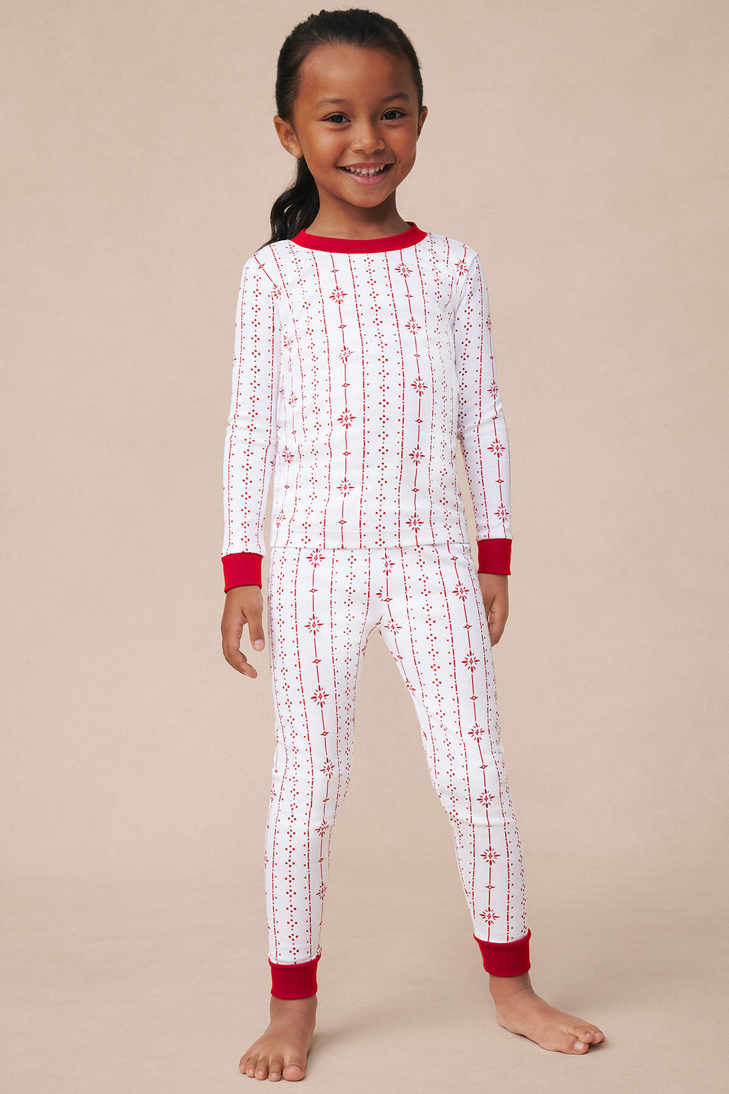 Child wearing white long-sleeve pajama set with red snowflake and stripe pattern, red ribbed cuffs and neckline.