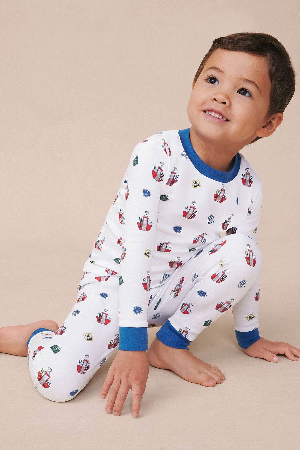 Child wearing white long-sleeved pajama set with ski lift print and blue ribbed cuffs and neckline.