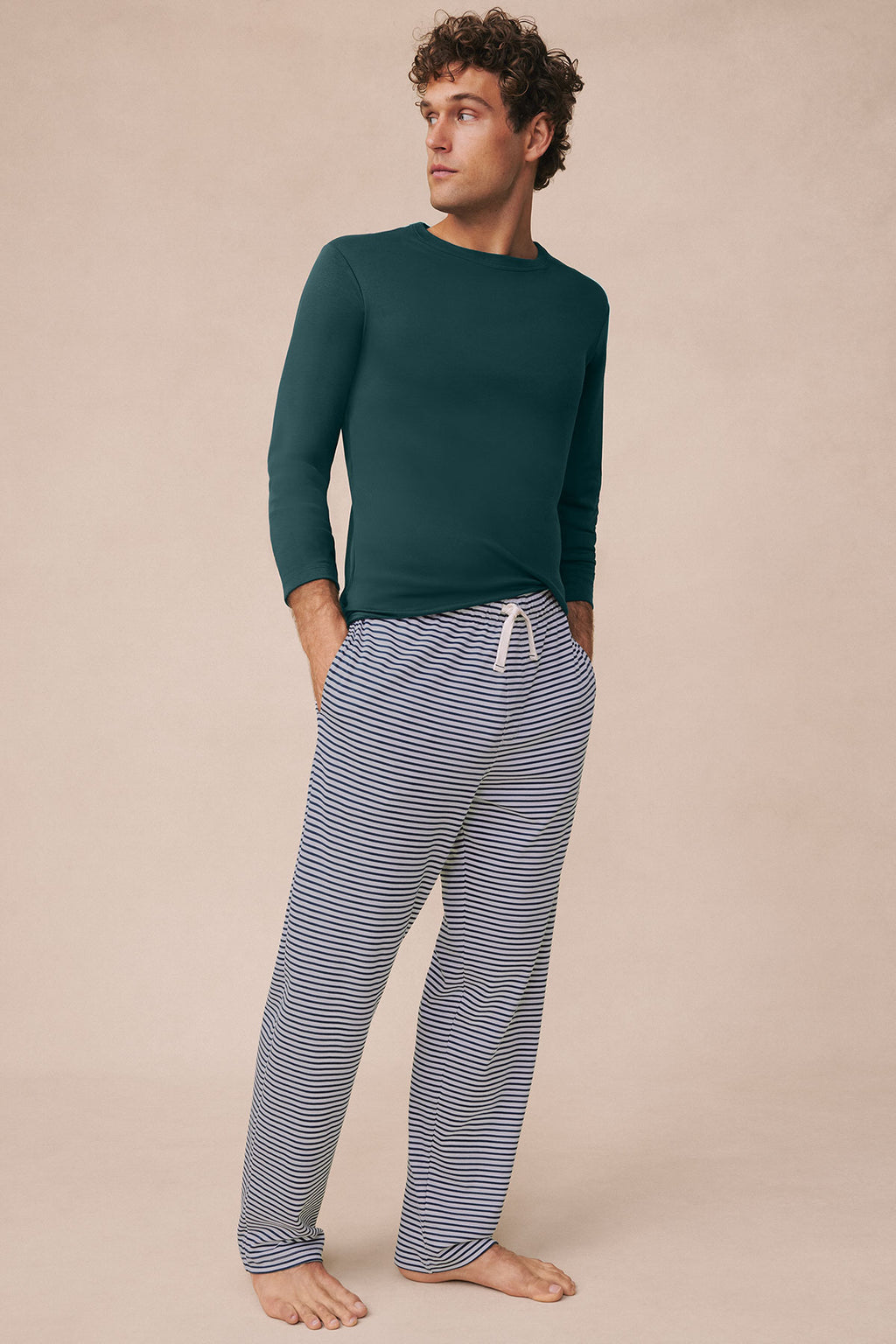 Man wearing dark teal long-sleeve shirt and striped pajama pants with drawstring waist.