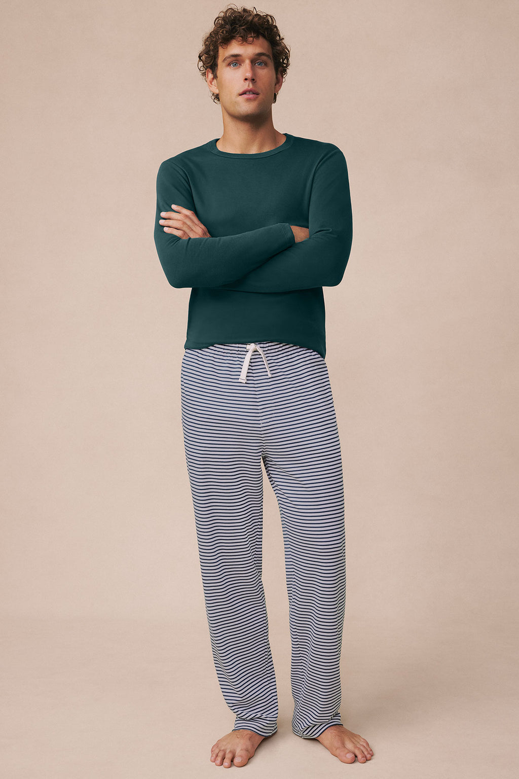 Man wearing dark teal long-sleeve top and striped navy blue pajama pants with drawstring waistband.