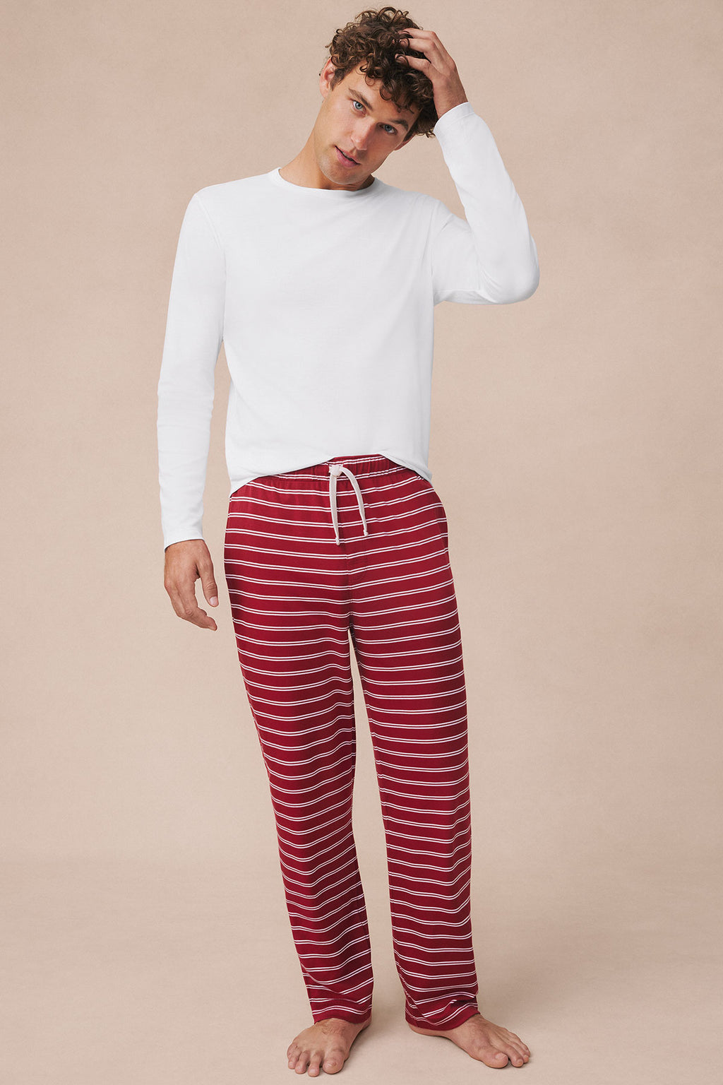 Man wearing white long-sleeve top with red and white striped pajama pants.
